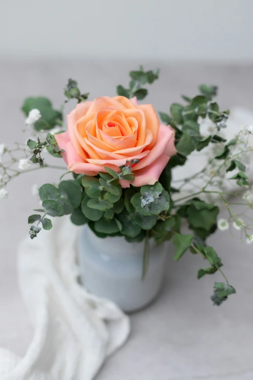 an orange rose on a table with leaves and greenery