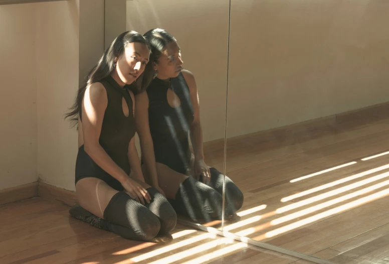 two women sit on the floor near a mirror