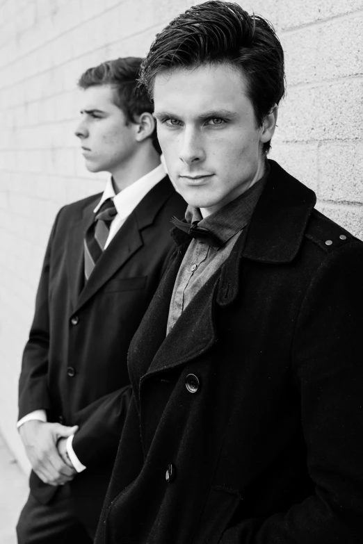 two men in coats and ties are standing near a wall