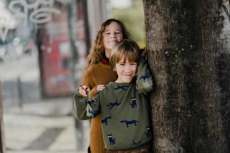 two young children are hugging each other, one is wearing brown