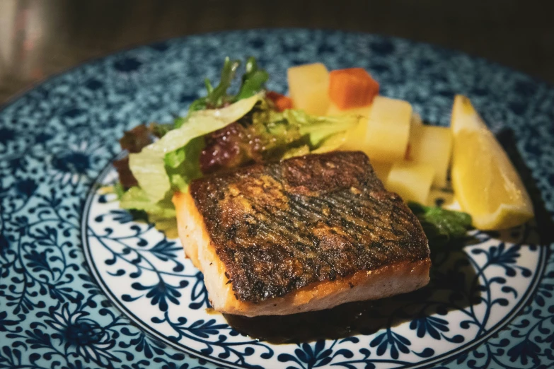 a piece of meat and a pile of mixed vegetables on a blue and white plate