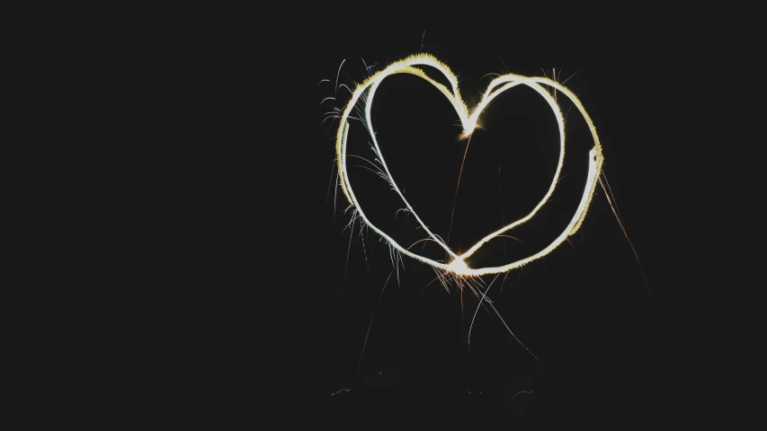 a pair of hands hold sparklers while making the shape of a heart