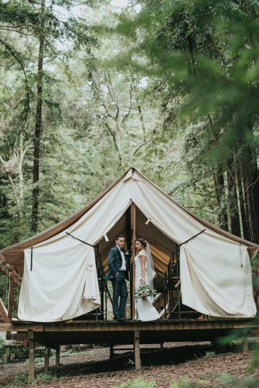 a man and woman standing in a tent surrounded by trees