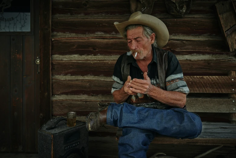 an older man with a cowboy hat sitting in front of a log wall