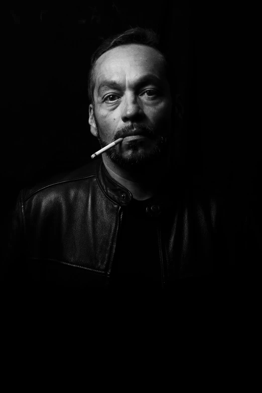 black and white po of man in leather jacket smoking a cigarette