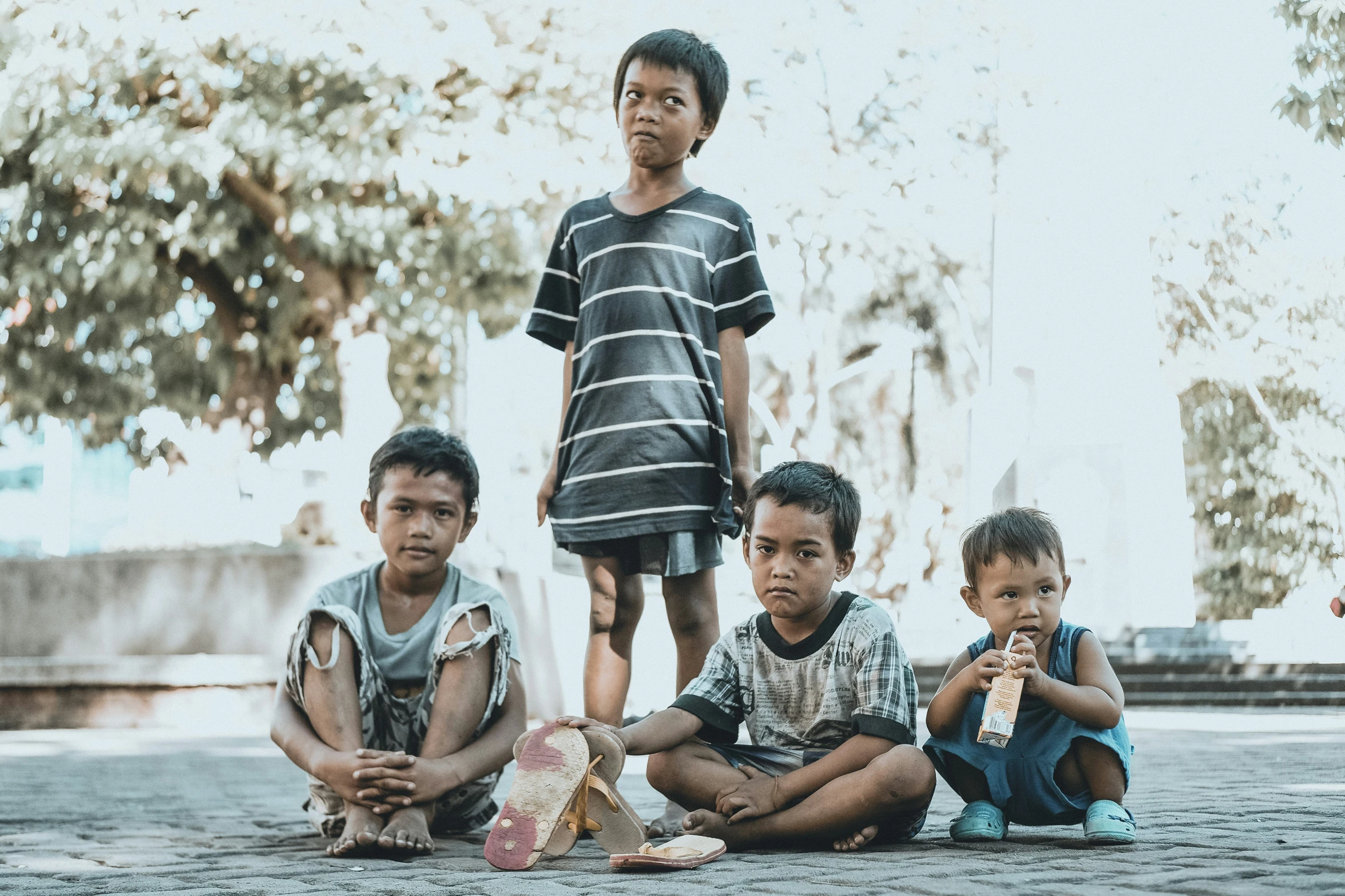 three young children standing and sitting on the ground