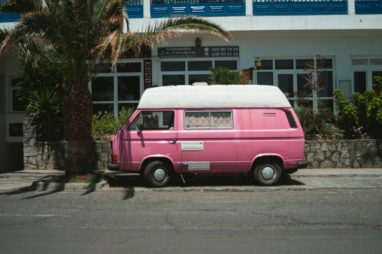 a pink and white van is parked by the side of a road