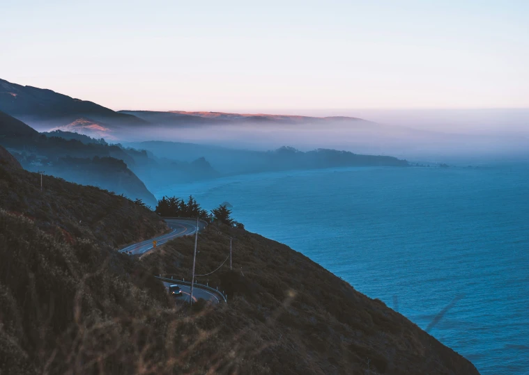 a long and winding road on a hill side with water in the background