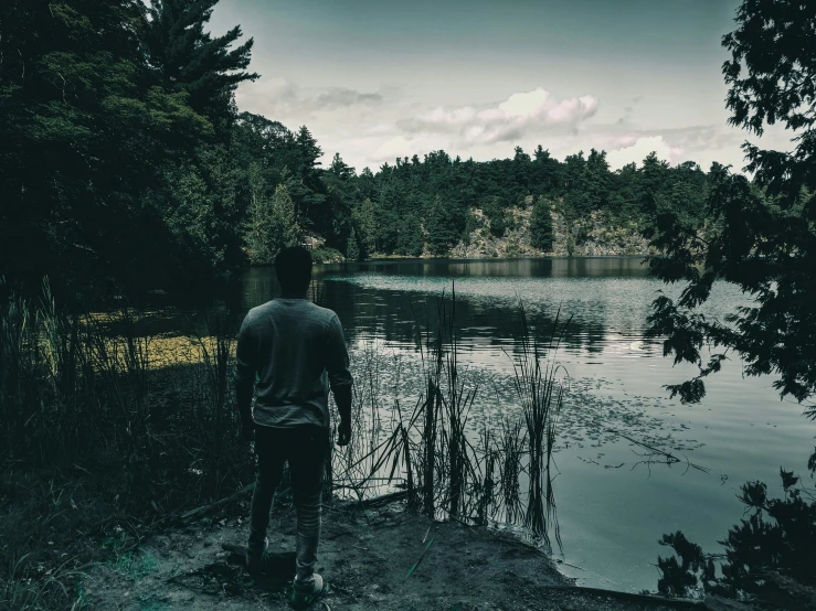 man standing on the edge of a lake looking in to a forest