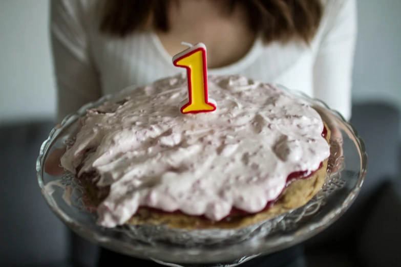 a young person holds up a cake with a candle