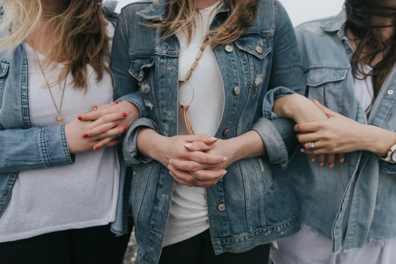 three women wearing jackets and holding hands close together