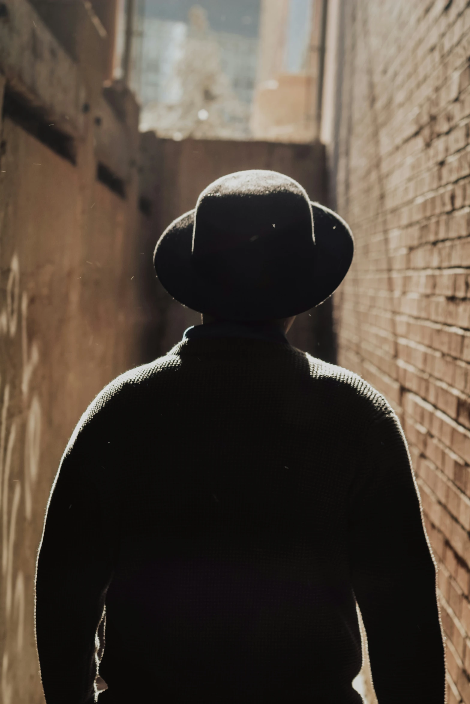 back view of person wearing a fedora walking down a street
