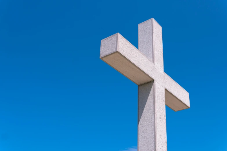 a cross standing in front of a blue sky