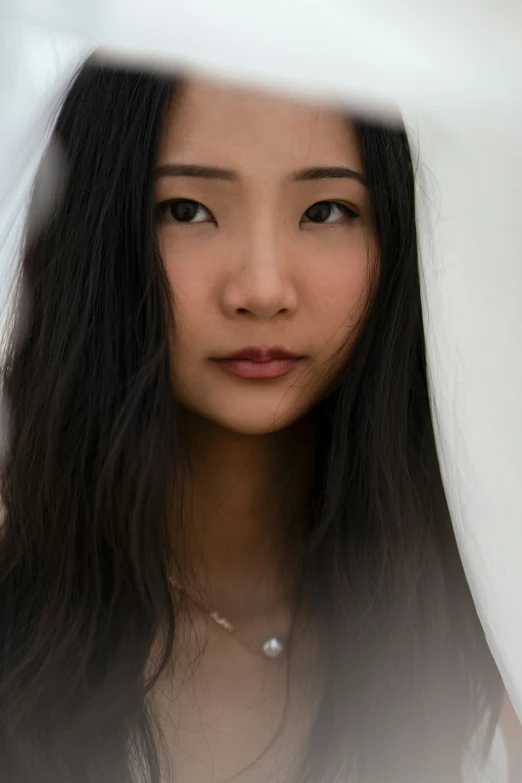 an asian girl in a dress poses under the white fabric