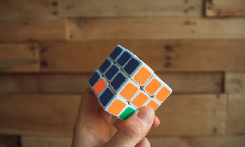 a hand holding a colorful cube against a wooden wall