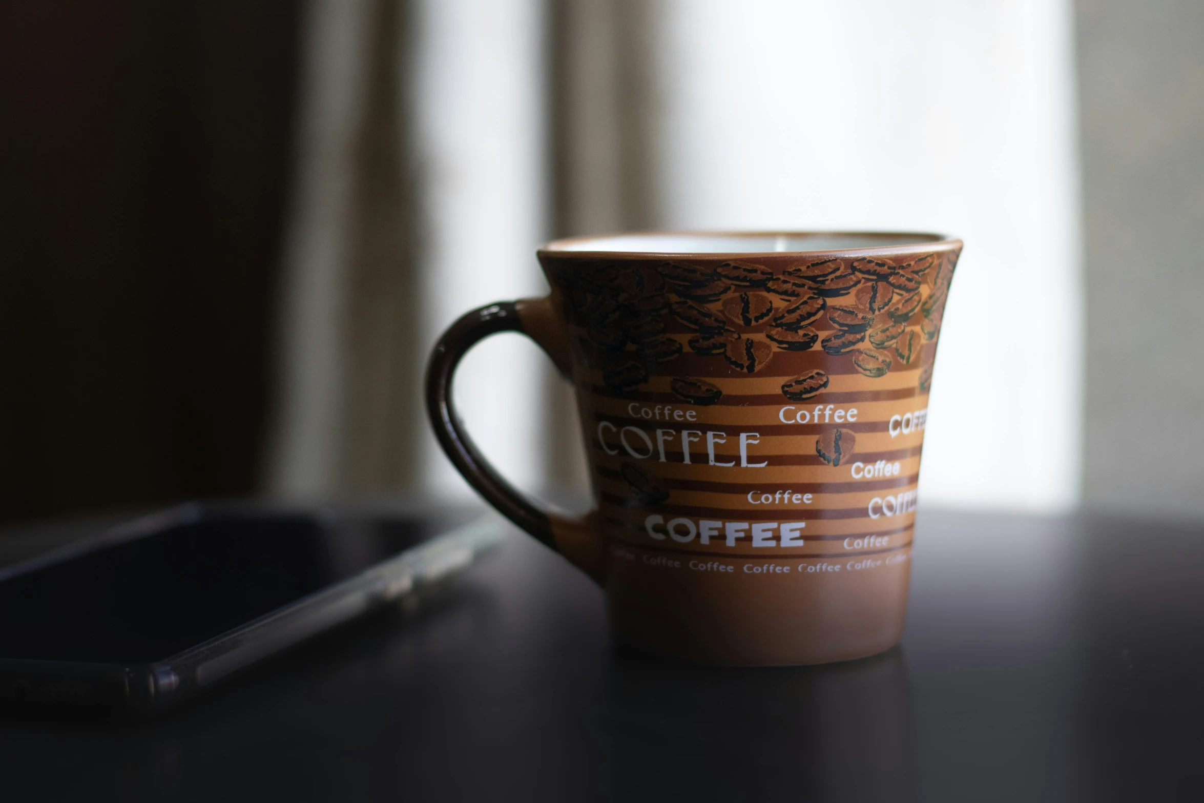 a brown coffee mug on a table next to a phone