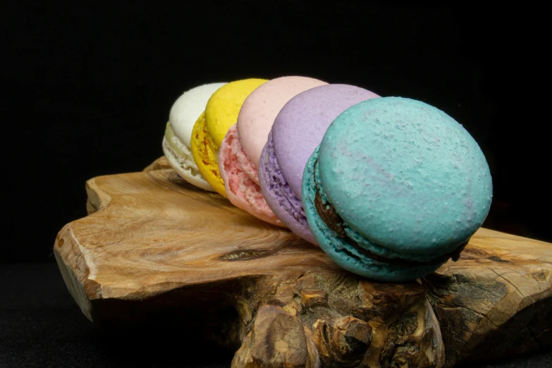five multicolored macarons sitting on top of a wood log