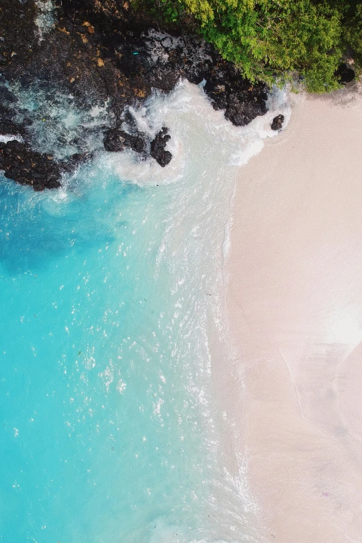 a sandy beach next to a turquoise water and rocks