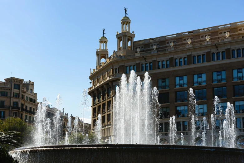 the fountain with many water jets is surrounded by buildings