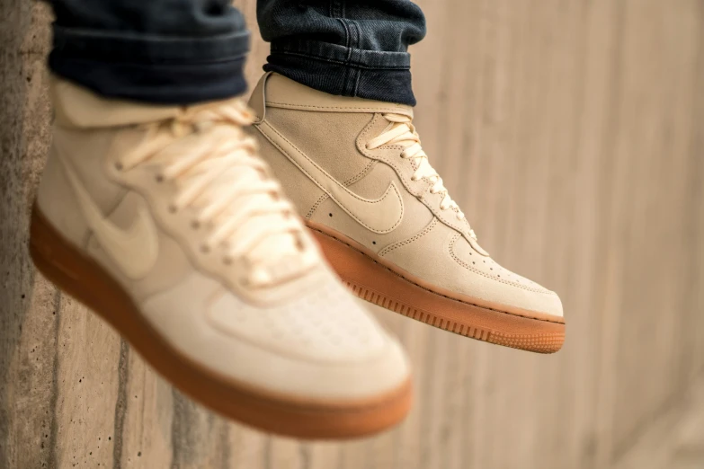 someone wearing brown sneakers standing up against a wood wall