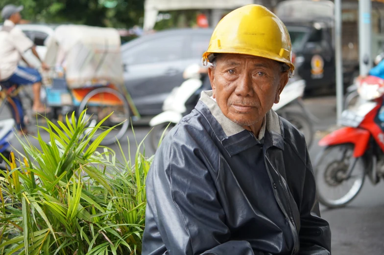 an old man with a yellow helmet is sitting