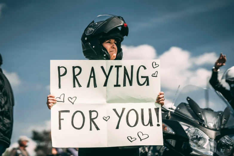 a man holding up a sign reading praying for you