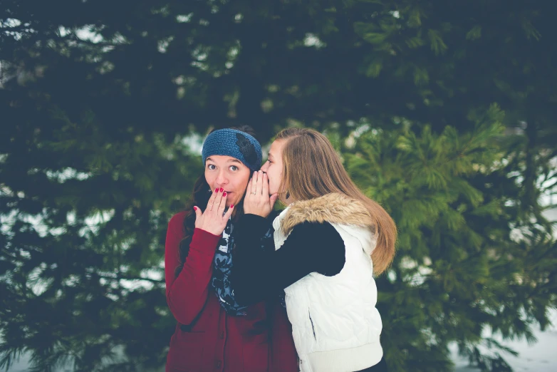 two girls with their mouths open standing under a tree