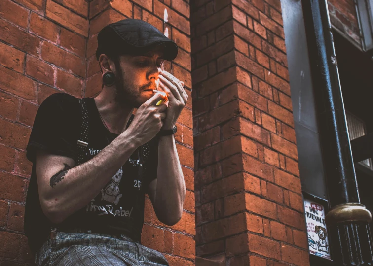 a man standing near a brick wall holding a cigarette