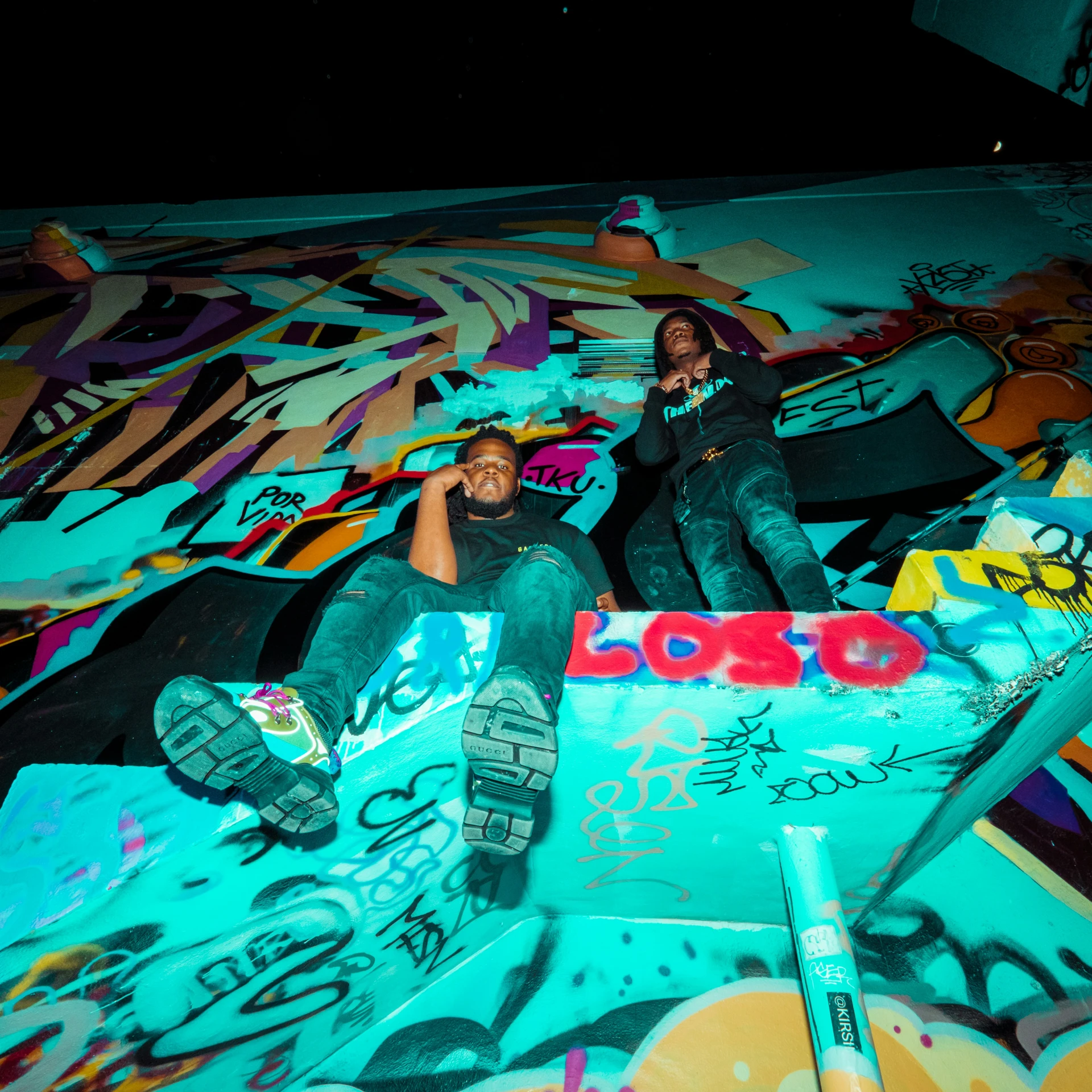 two young people sitting on a graffiti covered wall