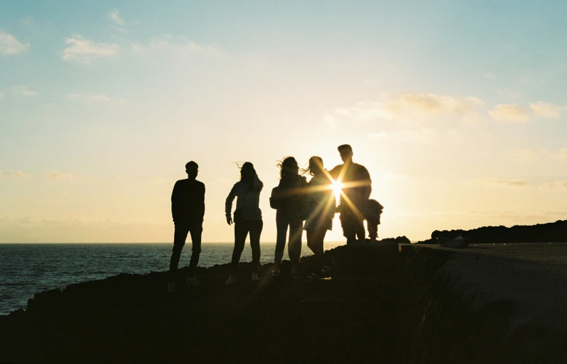 four people standing near the water looking at the sun