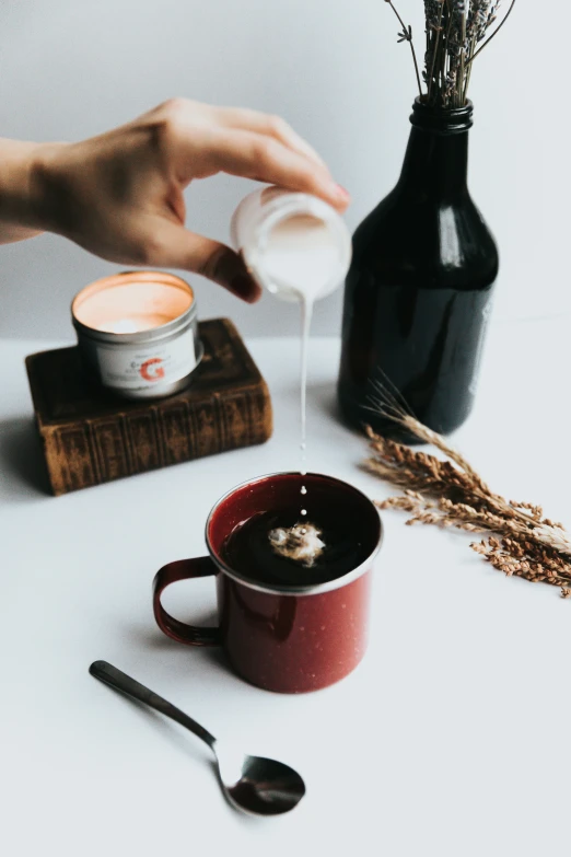 a persons hand pouring sugar into coffee in a red cup