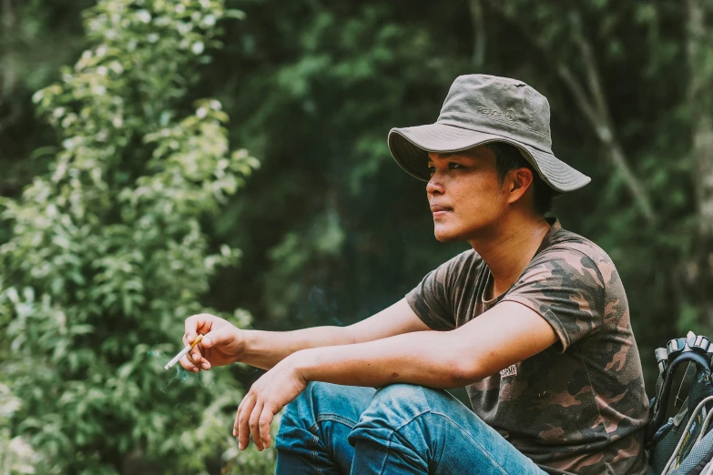 man sitting on motorcycle while smoking cigarette in forest