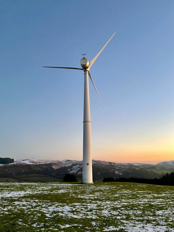 the sun is setting behind two windmills in the field