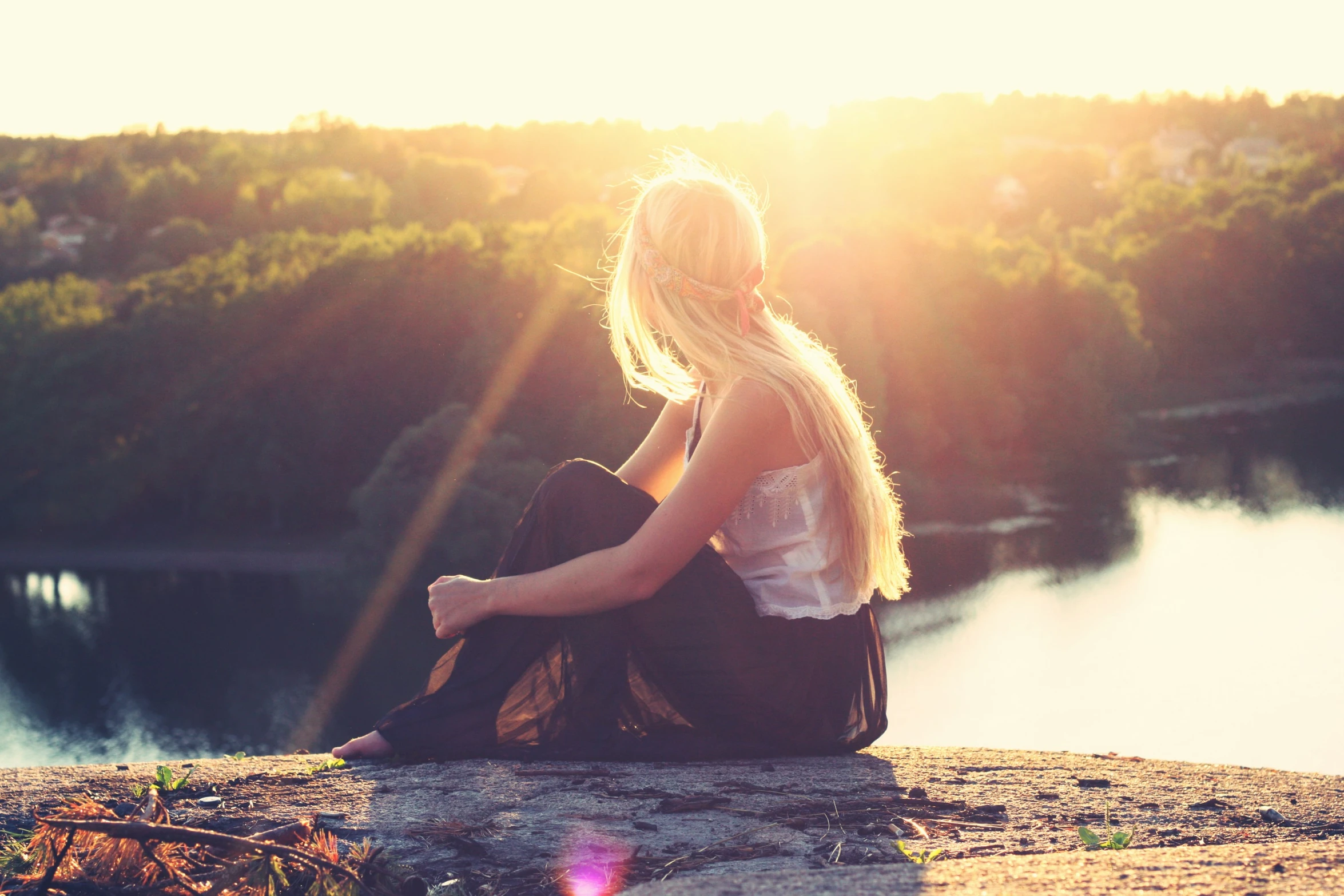 a woman sitting on top of a rock next to water