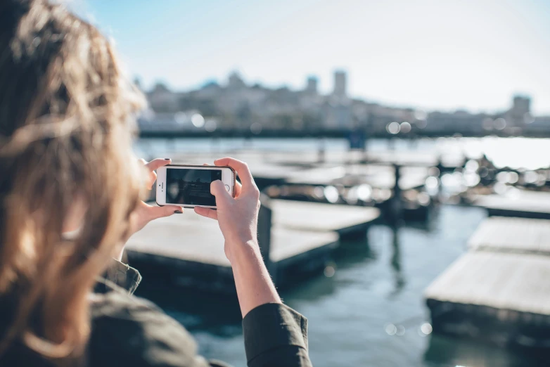 woman with long hair holding up a smart phone looking at the pier