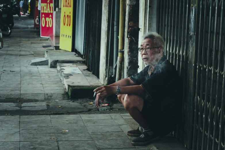 a man sitting on the sidewalk smoking and looking away from us