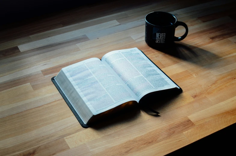 a cup of coffee, an open book and an open book sit on a wooden table