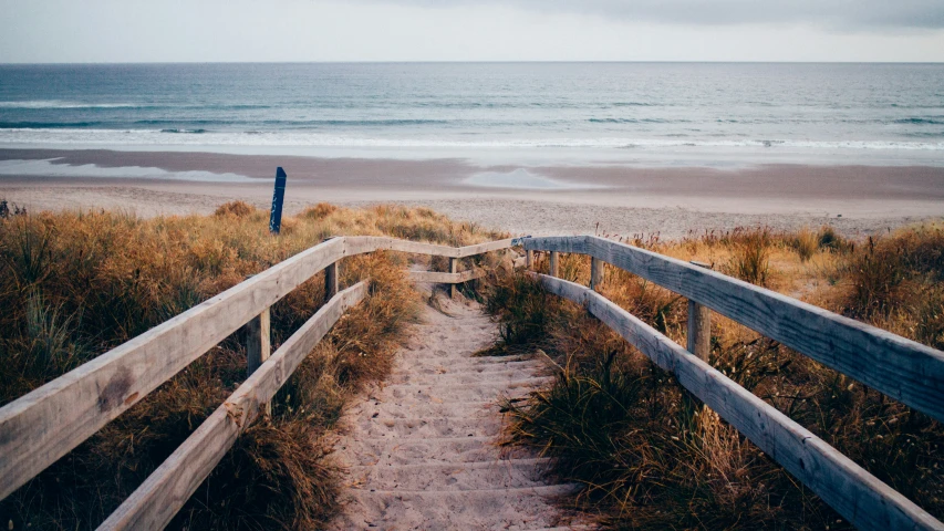 two people standing at the end of a wooden walkway leading to the ocean