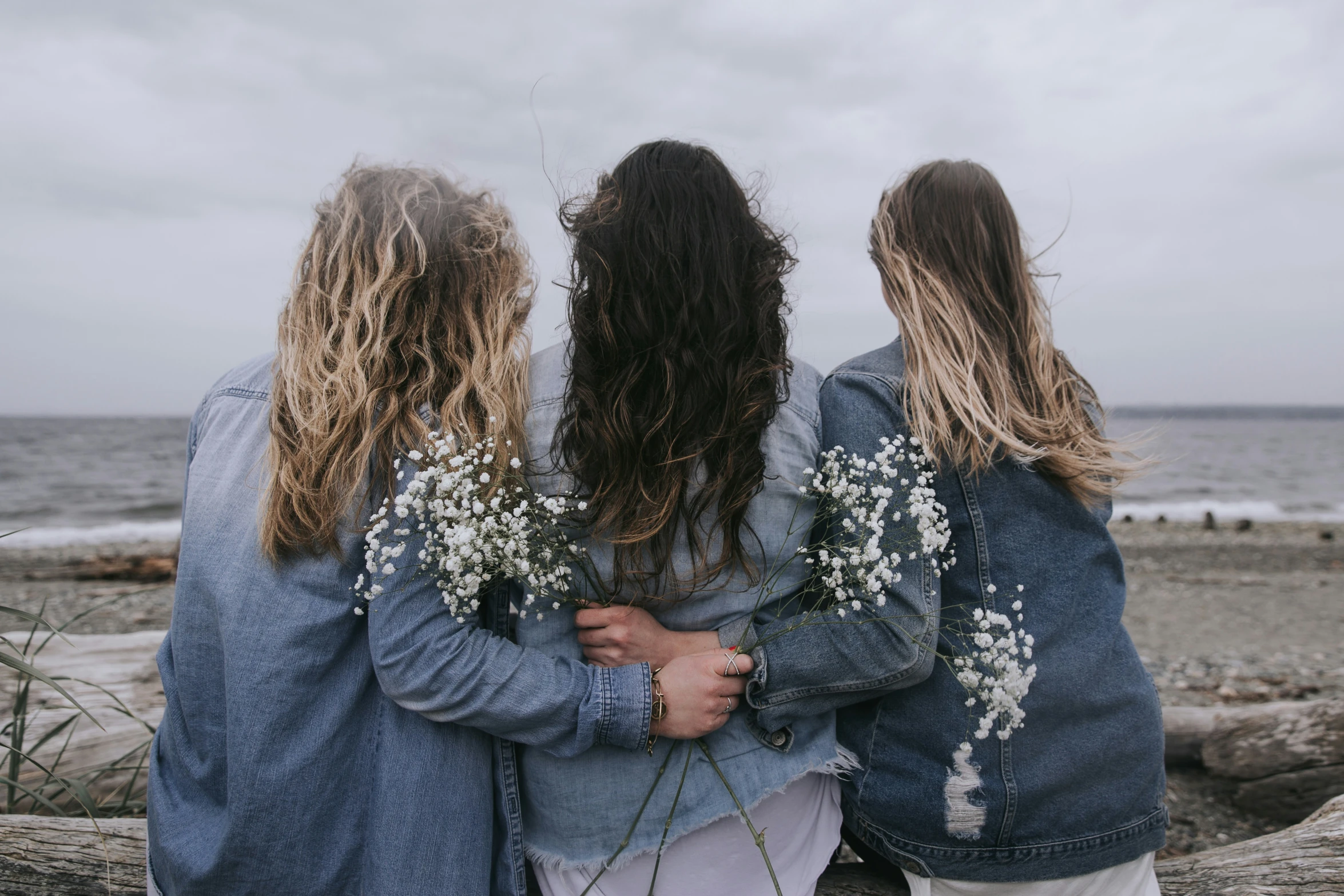 three women stand close together looking out to sea