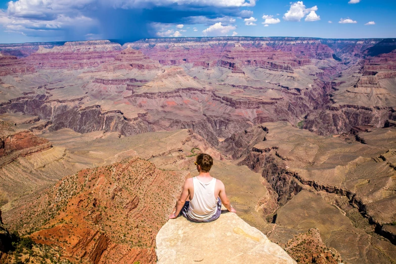 person sitting on top of a cliff in front of a vast canyon
