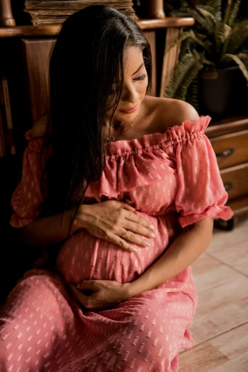 a young pregnant woman in pink dress on a bed