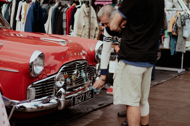 a man looking at the front end of a red classic car