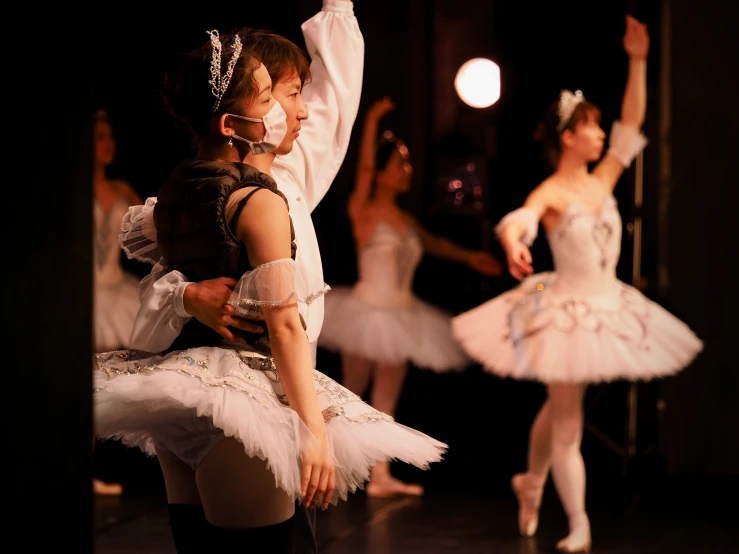 a child in white holds the arm of a ballet instructor