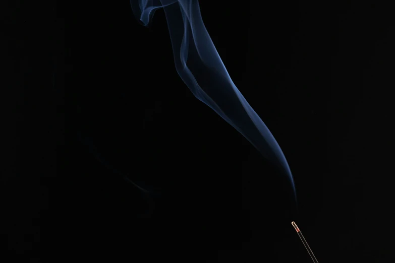 a lit matchstick and some smoke in the dark
