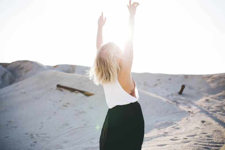 woman raising her hands high on a sandy beach