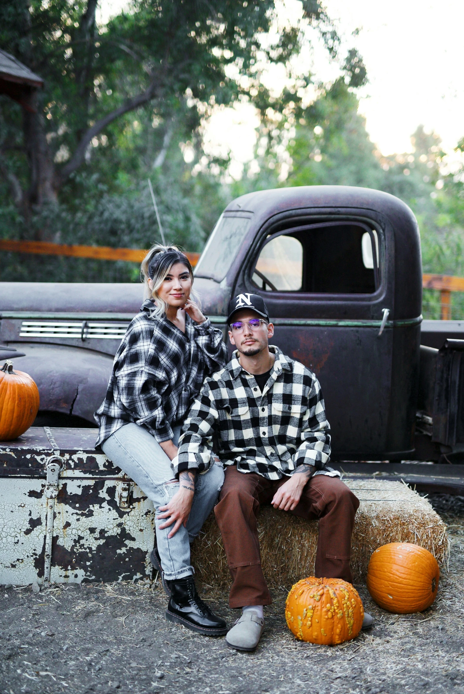 a man and woman are sitting on a hay bale next to an old truck