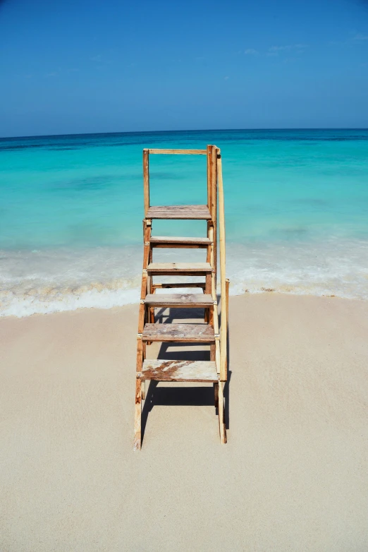 ladder made out of wood on a beach with the ocean behind it