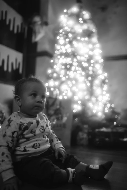 a baby sitting in front of a large christmas tree