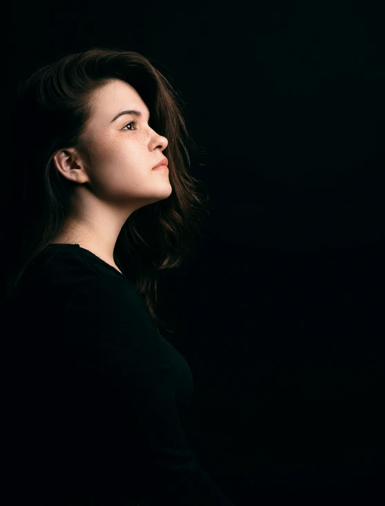 a beautiful young lady standing in the dark with a black background