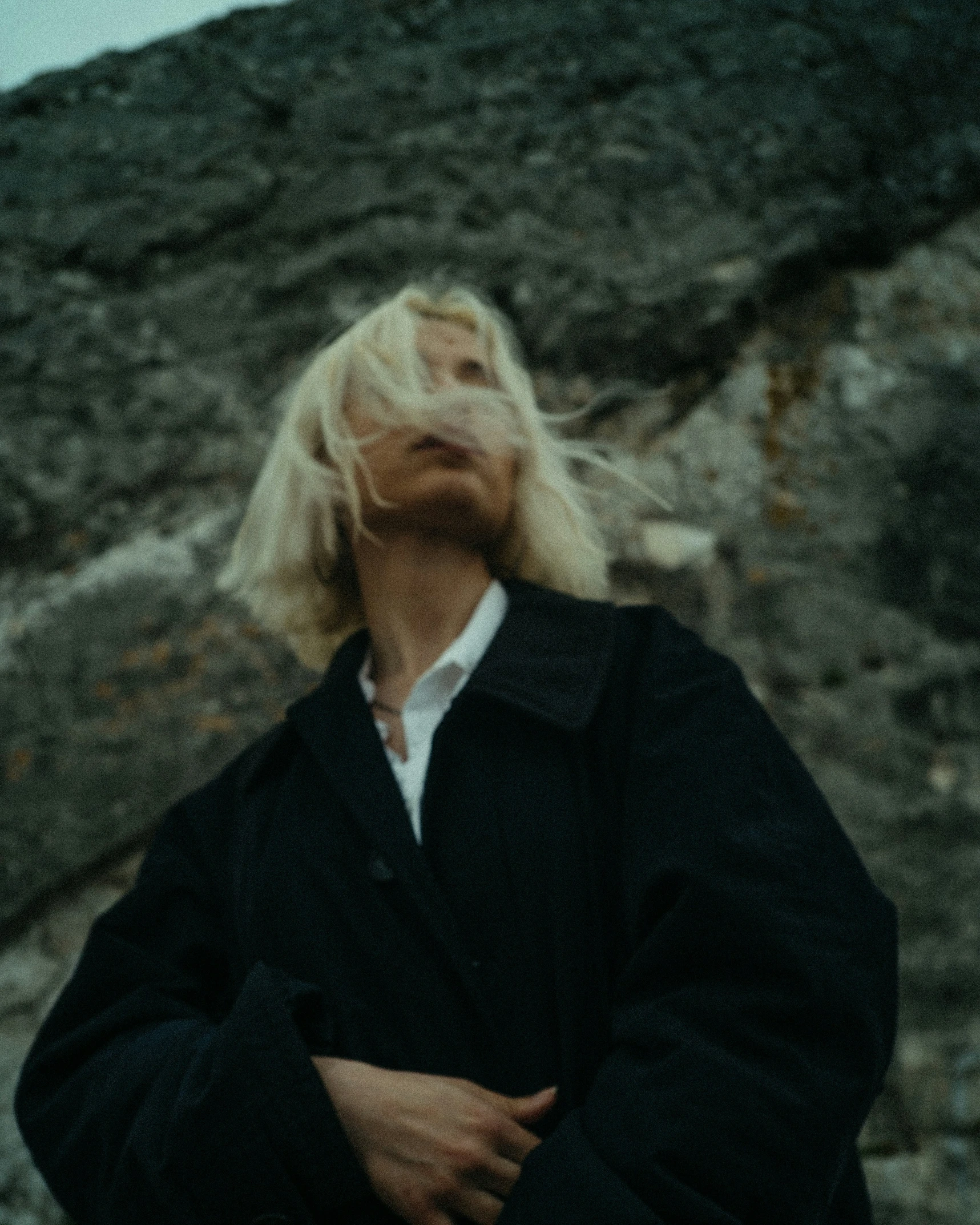 woman with blonde hair standing in front of rocky area